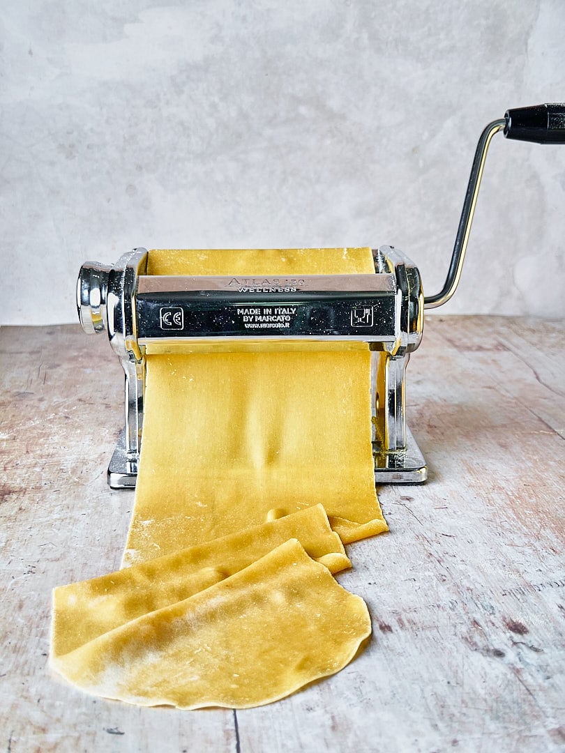 Abbildung von einer frischen Pasta-Teigplatte, die mit einer Nudelmaschine ausgerollt wird.