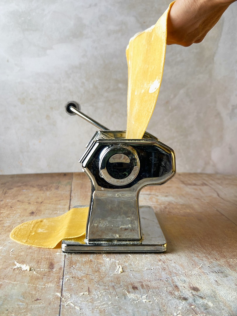 Abbildung von frischem Pastateig, der durch eine Nudelmaschine gerollt wird.