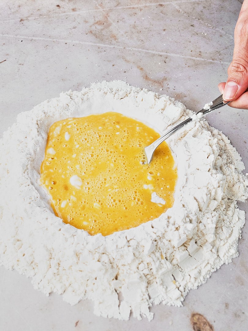 Using a fork to mix eggs and flour to make pasta dough.