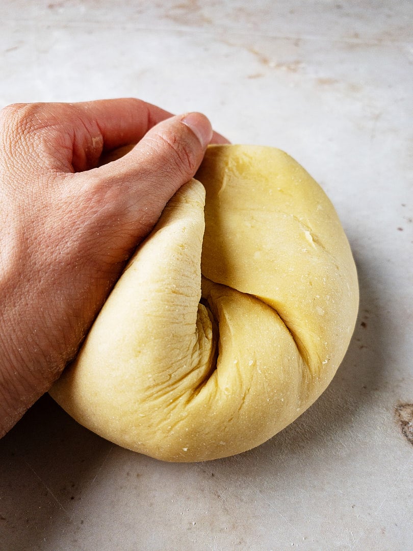 One female hand kneading a fresh pasta dough ball on a marble tabletop.