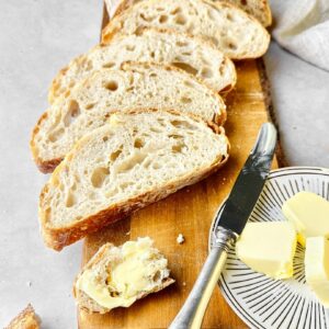Sliced loaf of freshly baked sourdough bread with a small plate of butter on the side.