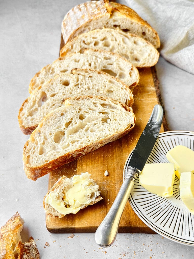 Sliced loaf of freshly baked sourdough bread with a small plate of butter on the side.
