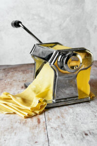 rolling fresh pasta dough through a pasta machine.