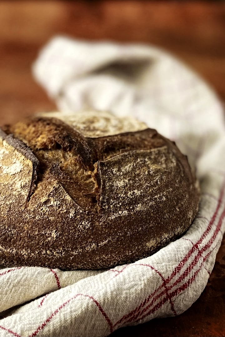 Close-up of a dark whole wheat sourdough bread on a white tea towel.