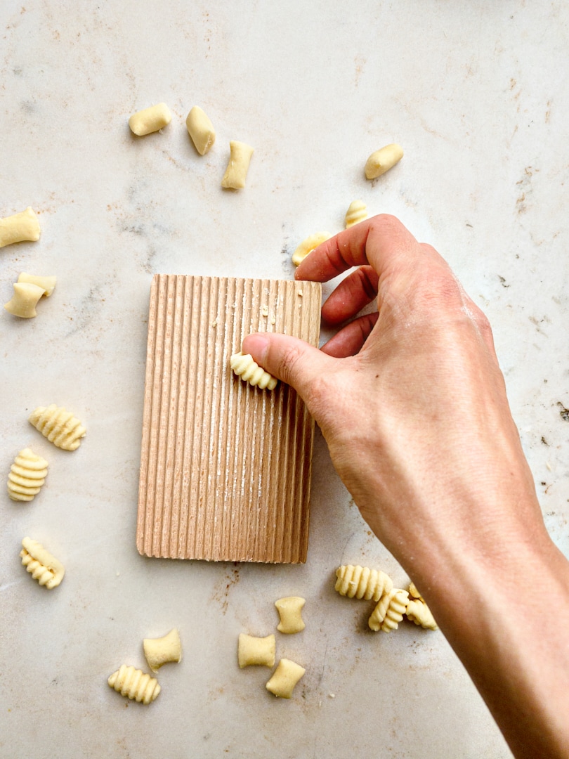 Zubereitung von handgemachten Malloreddus: Ein kleines Teigstück wird mit dem Daumen über ein Gnocchi-Brett gerollt, um der Pasta die charakteristischen Rillen zu verleihen.