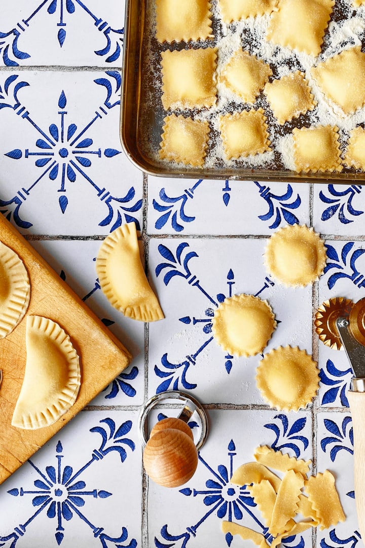 Different shapes of homemade ravioli on a white and blue tile backdrop.