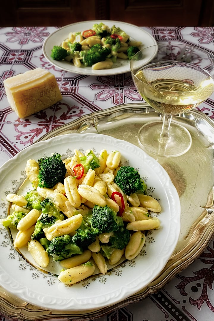 Homemade cavatelli and broccoli pasta on a silver serving tray with a glass of white wine.