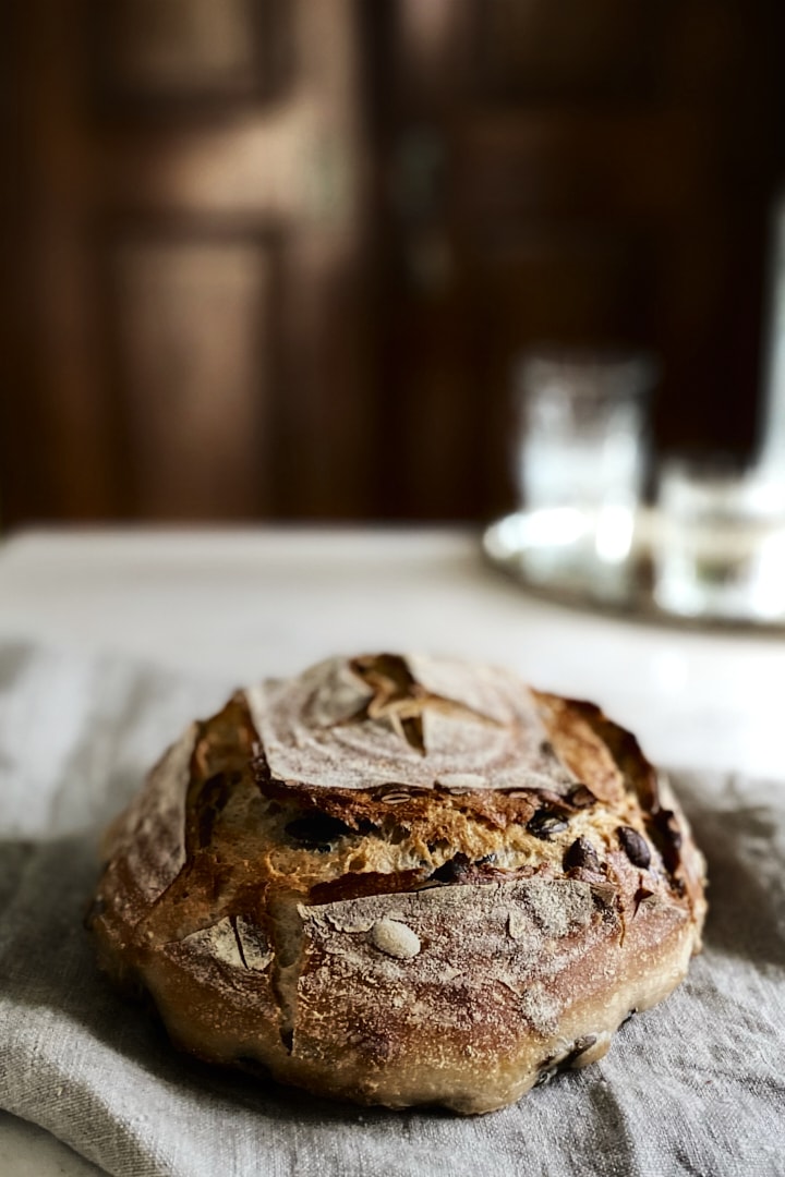 A loaf of sourdough on a marble table in front of a dark wooden door.