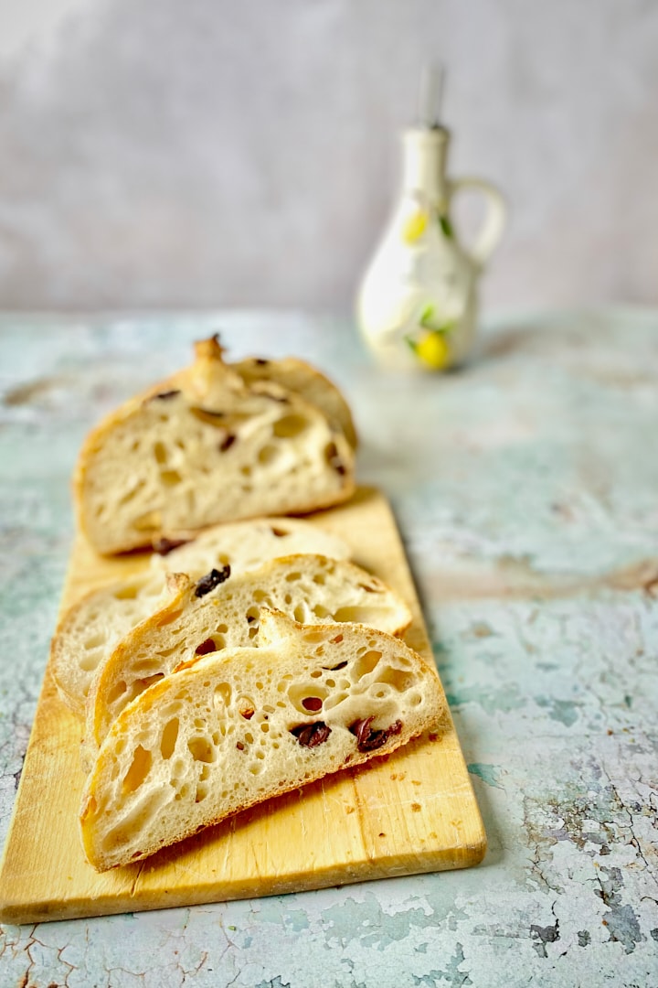 Sourdough olive bread on a wooden board with a bottle of olive oil in the background.