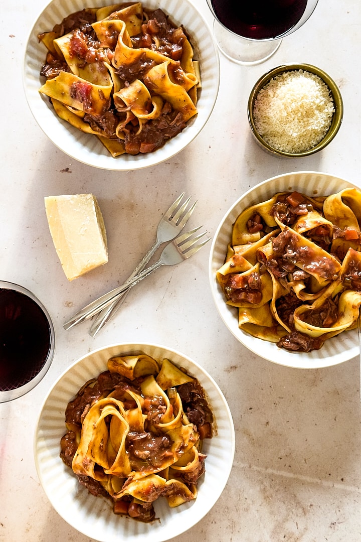 Three bowls of pappardelle served with lamb ragu and feshly grated parmesan cheese.