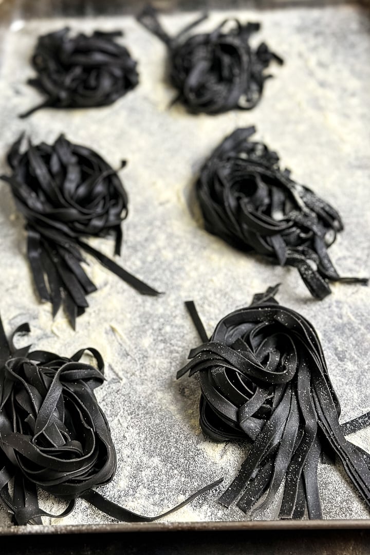 Six squid ink pasta nests on a semolina dusted baking tray.