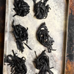 Flatlay of squid ink pasta nests on a baking tray.