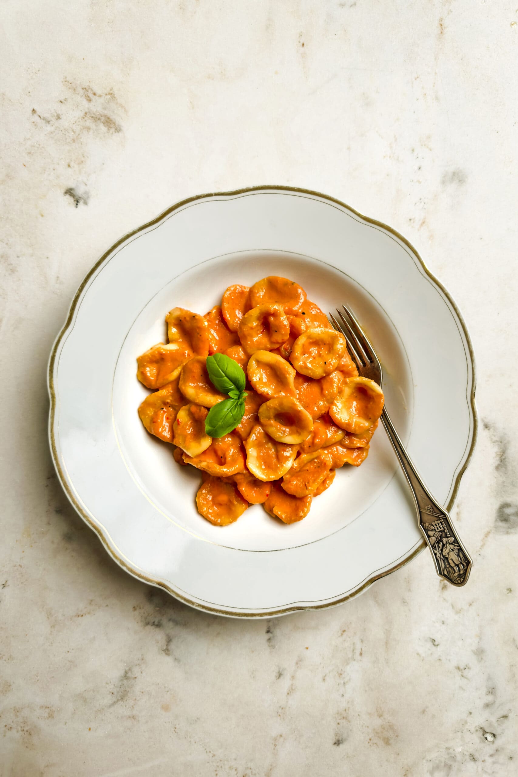 Orecchiette with creamy red pepper sauce on a white plate on a marble table. 