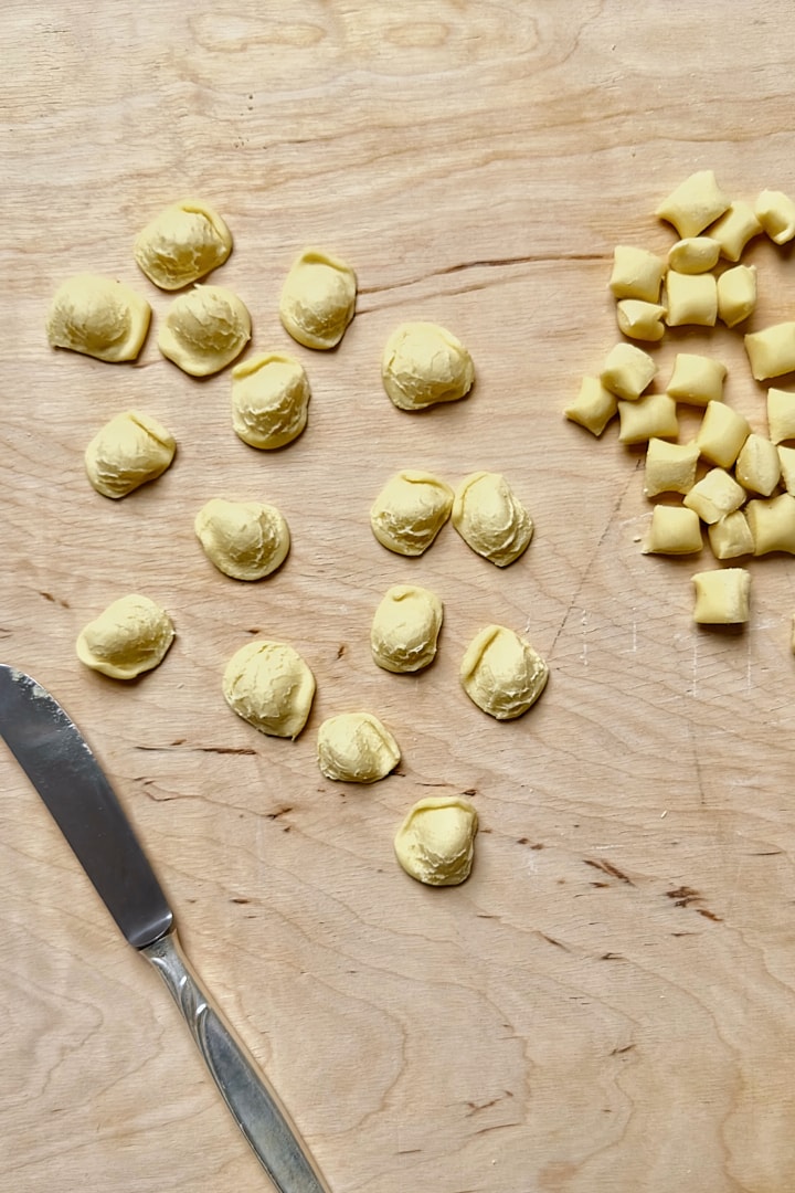 Making homemade orecchiette with a blunt knife on a wooden board.