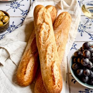 Three sourdough baguettes with cured meats, grapes and white wine on the side.