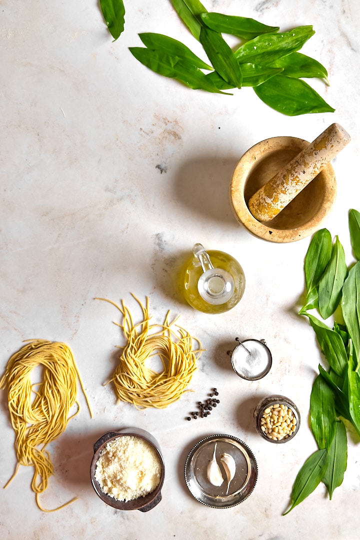 The ingredients and tools to make wild garlic pesto pasta: Wild garlic, fresh pasta, salt, pepper, pine nuts, parmesan cheese olive oil and a mortar and pestle.