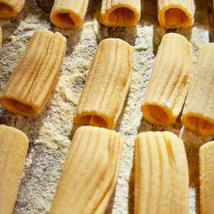 Fresh rigatoni pasta on baking tray dusted with semolina flour.