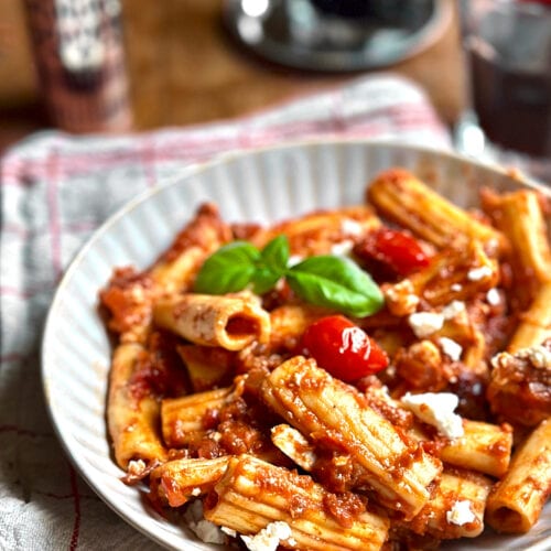 Rigatoni with aubergine ragu and two glasses of red wine next to it.