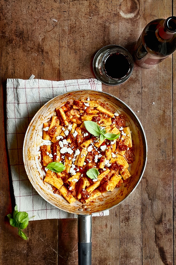 Fresh rigatoni with aubergine ragu in a pan on a rustic wooden table.