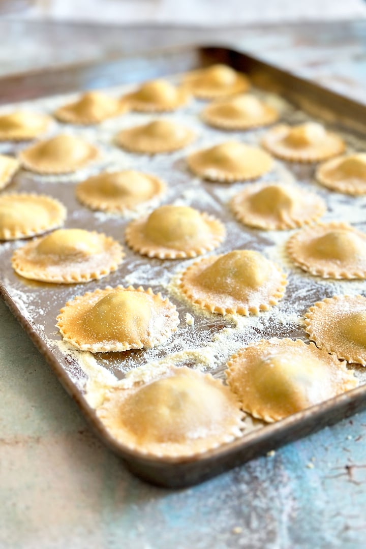A baking tray filled with homemade ravioli with asparagus-ricotta-filling.