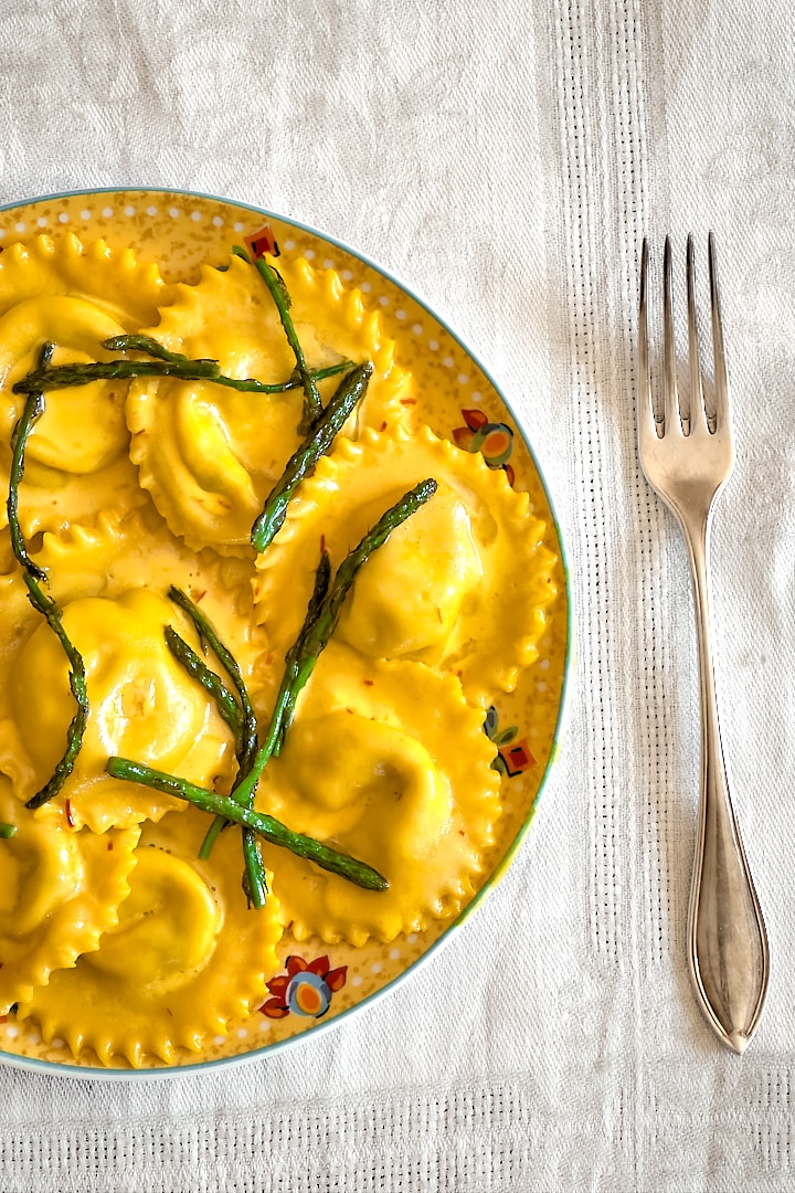 Homemade asparagus ravioli with golden saffron cream sauce on a yellow plate placed on a white tablecloth.