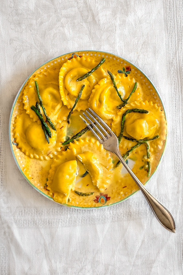 Asparagus ravioli in saffron cream sauce on a yellow plate with a fork.