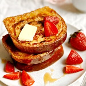 A stack of cinnamon swirl french toast with fresh strawberries on a white plate.