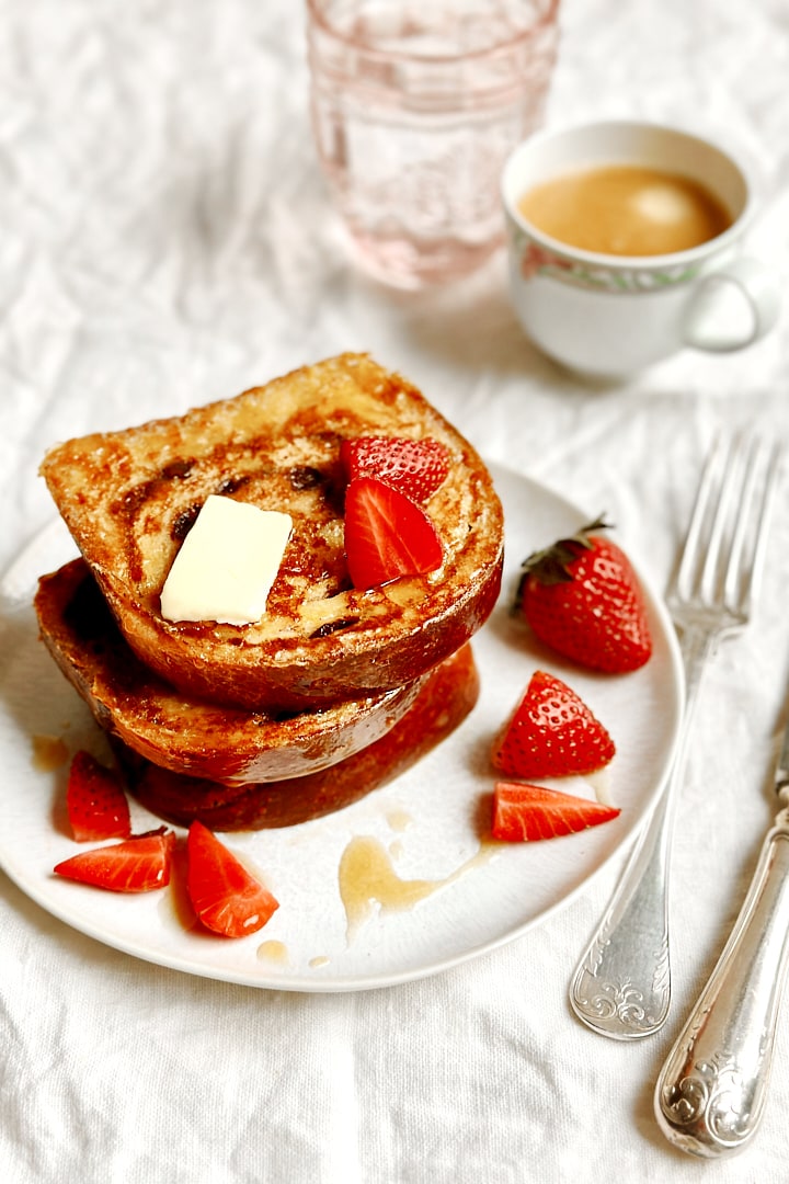 A stack of cinnamon swirl french toast and strawberries with a cup of coffee and a glass of water next to it.