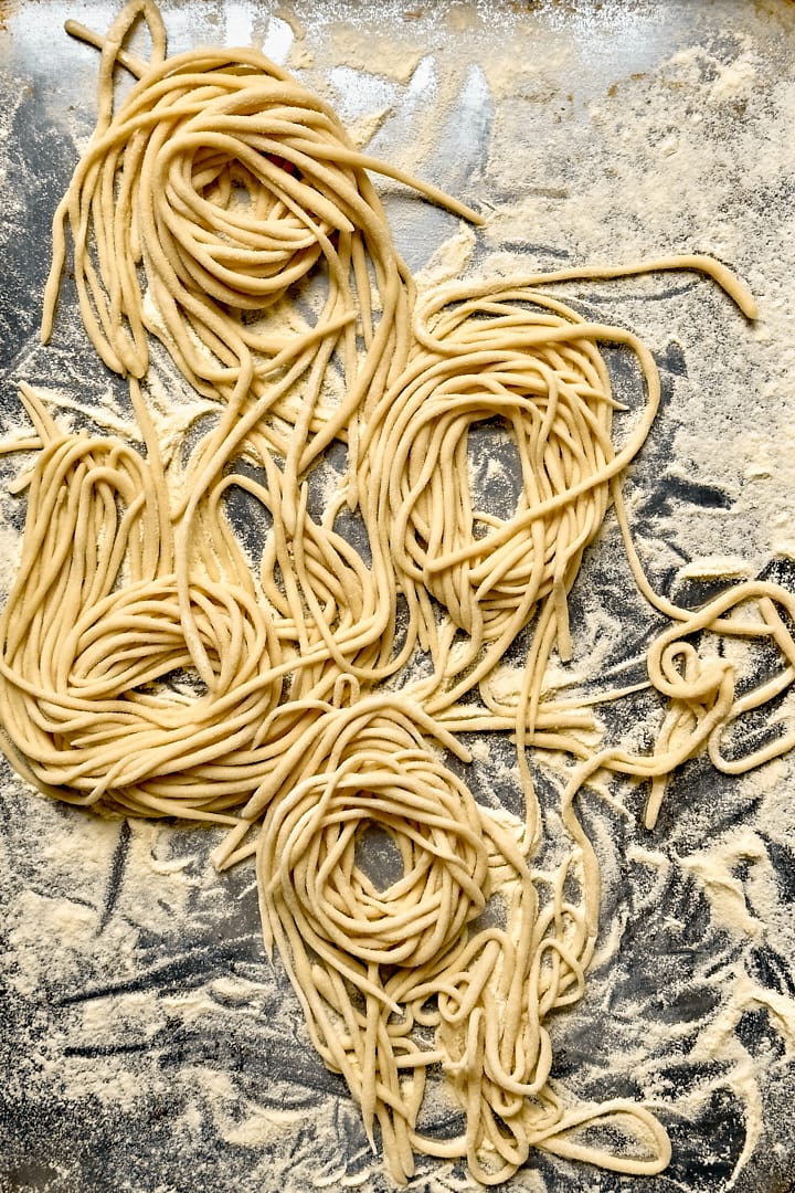 Homemade pici pasta nests on a baking tray dusted with semolina flour.