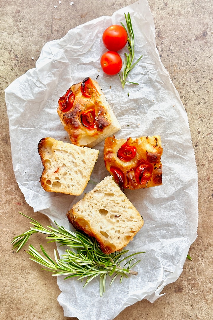 Four pieces of focaccia with cherry tomatoes and rosemary.