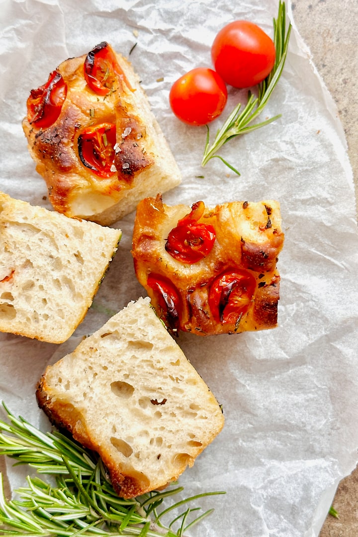 Sourdough focaccia with rosemary and cherry tomatoes on a piece of parchment paper.