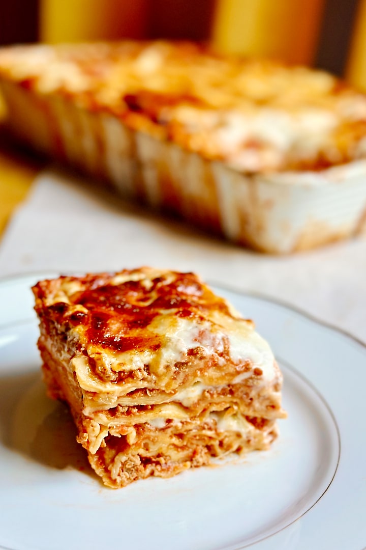 A baking dish with fresh lasagne and a plate with one portion of lasagne next to it.