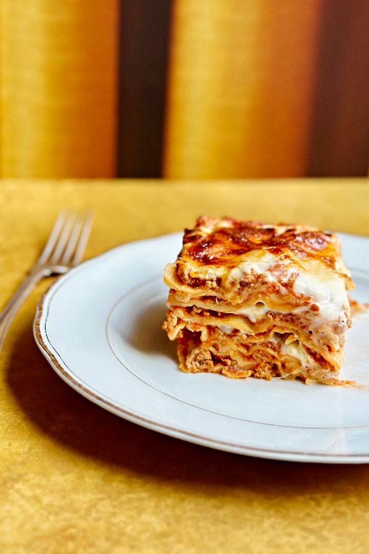 One portion of fresh lasagna al forno on a white plate with a fork next to it.