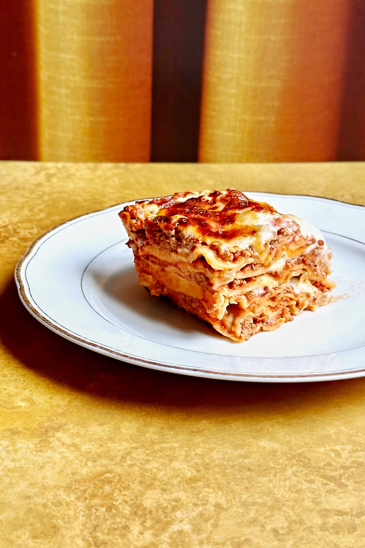 One portion of homemade lasagna al forno on a white plate.