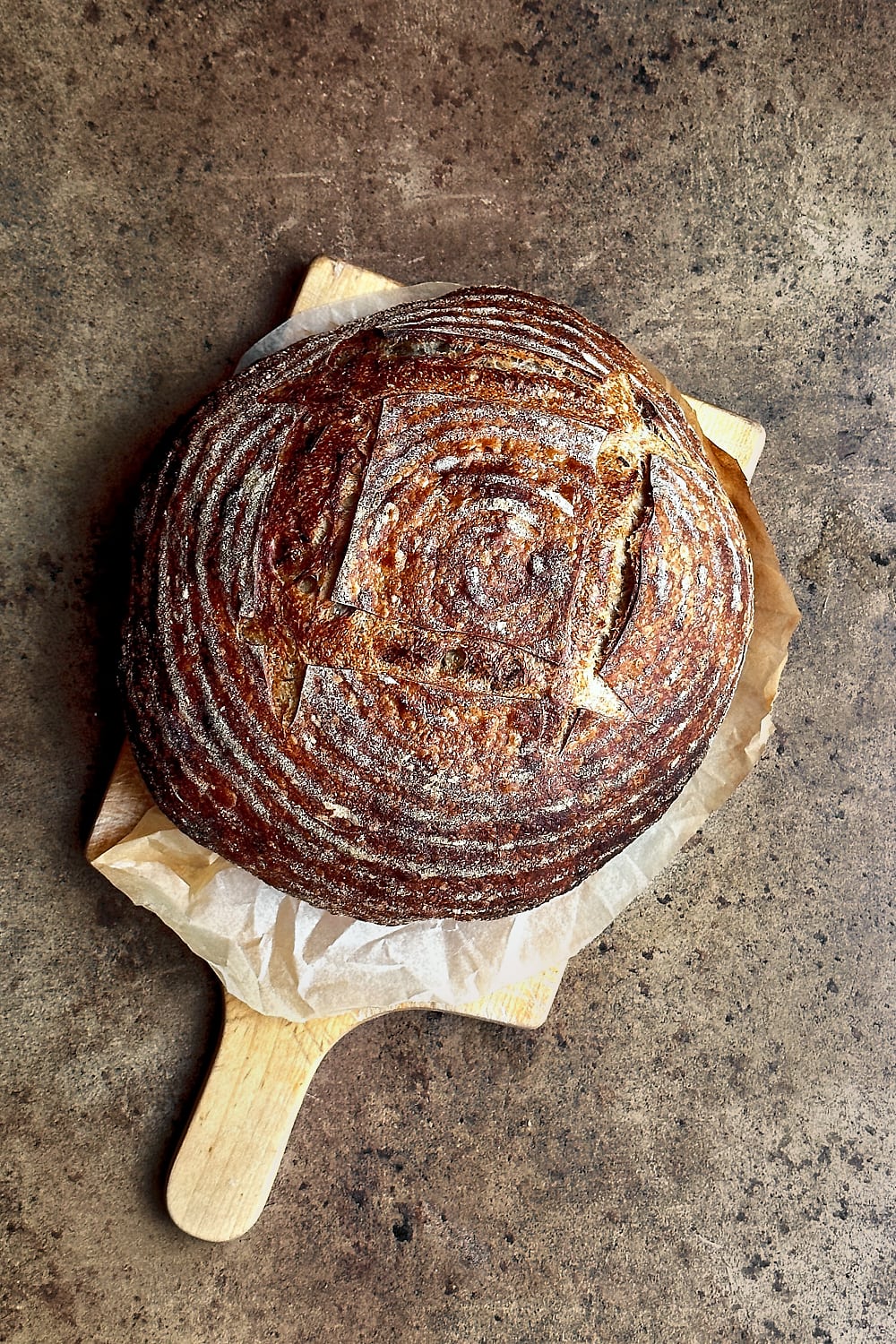 A loaf of roasted garlic sourdough bread on a wooden board.