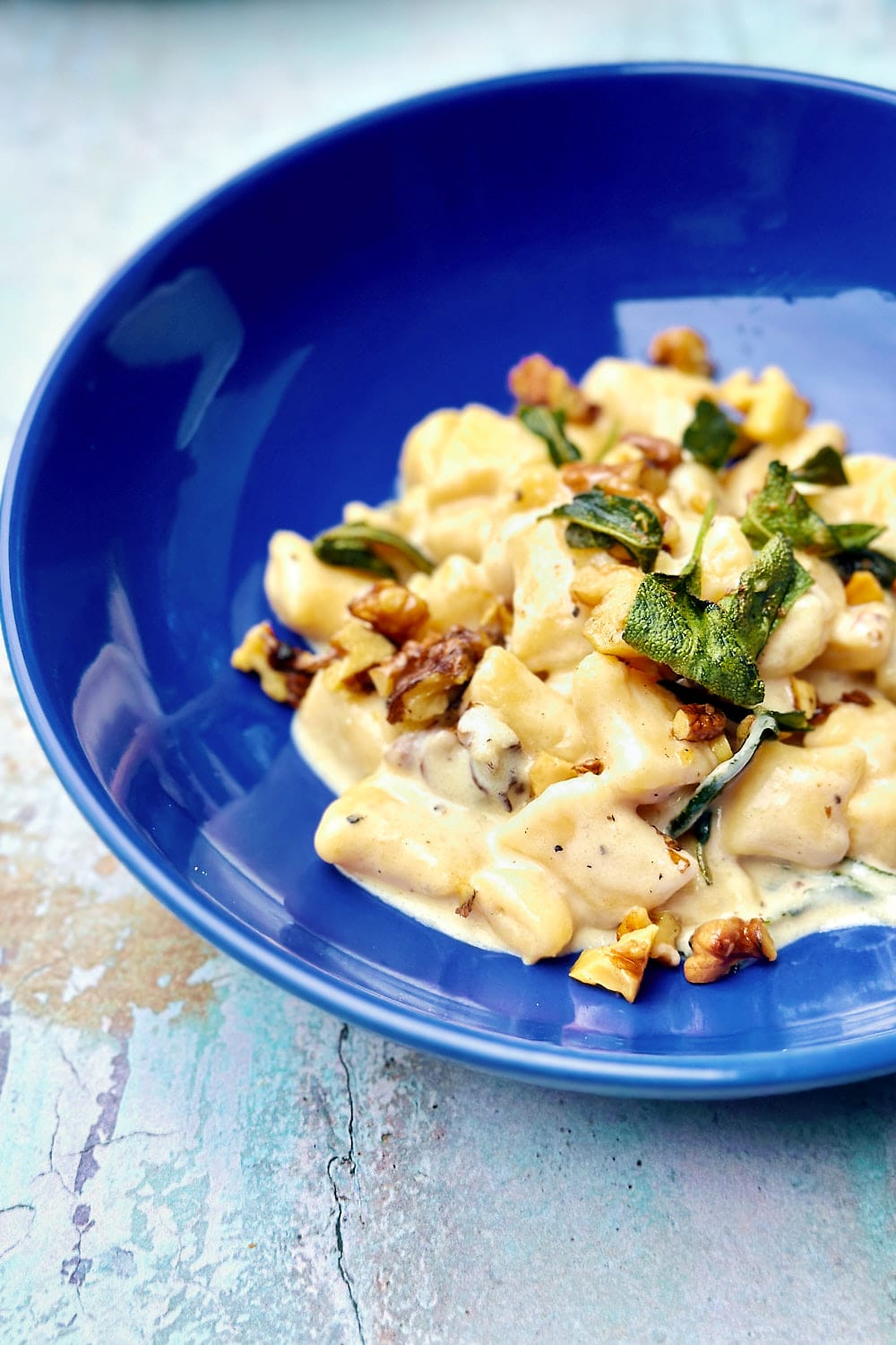 creamy gnocchi with walnuts and sage served on a dark blue pasta plate.
