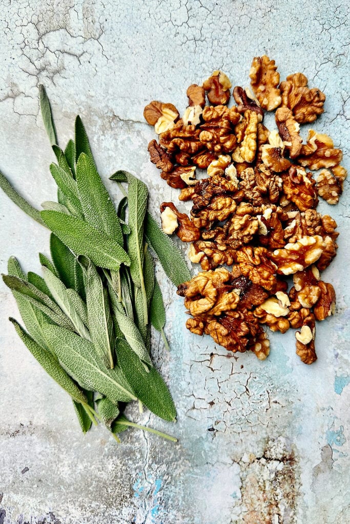 fresh sage leaves and chopped walnuts on a light blue wooden table.
