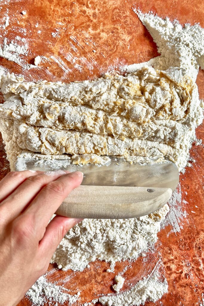 Using a bench scraper to combine the ingredients for homemade pasta dough.