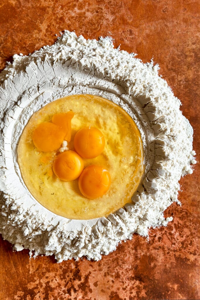 Four eggs cracked into a flour well to make fresh pasta dough.