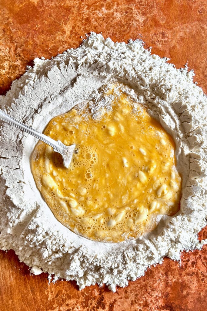 Scrambled eggs in the center of a flour well to make fresh pasta dough.