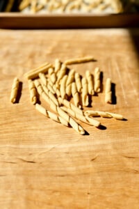 homemade busiate pasta in bright sunlight on a wooden pasta board.