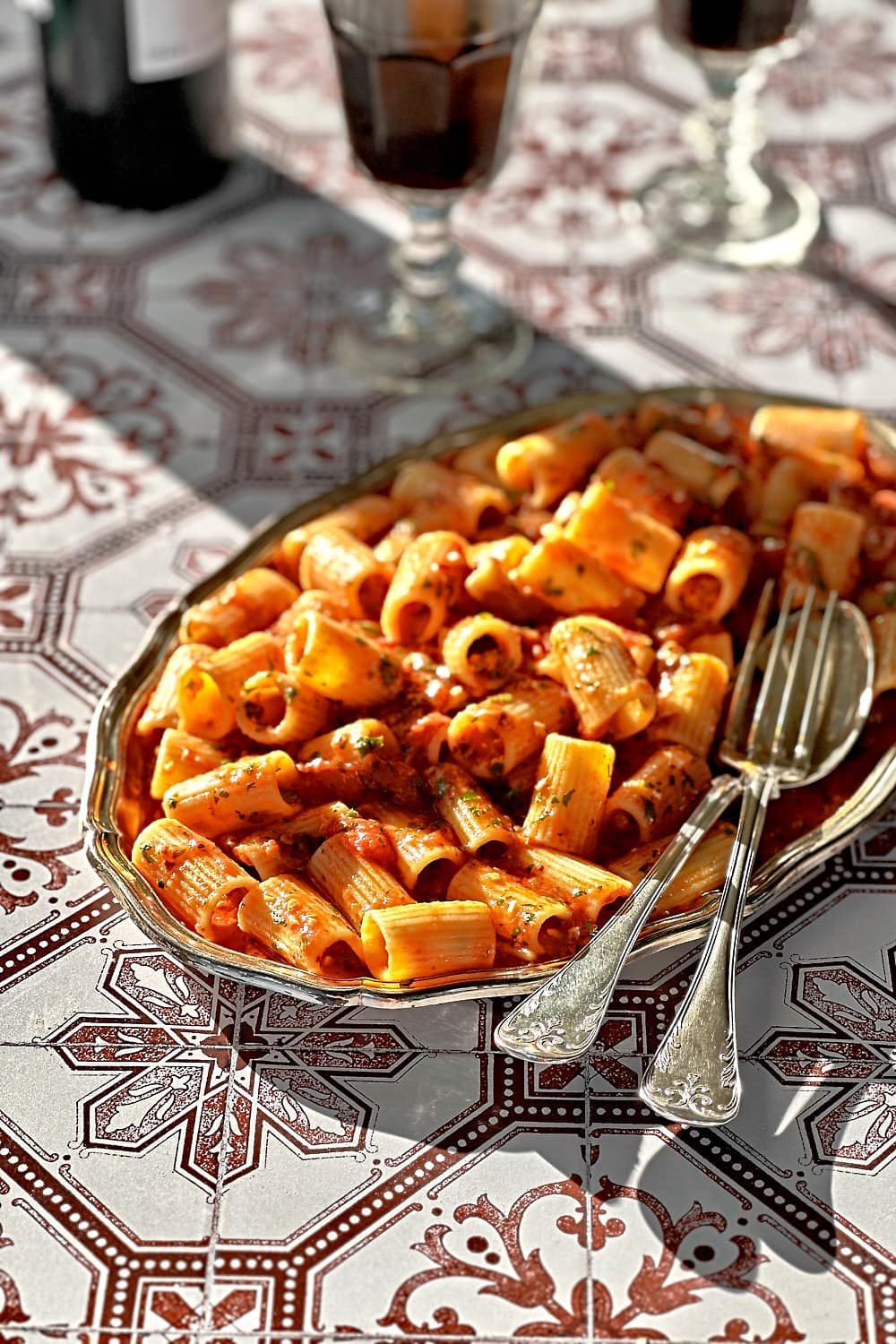 Rigatoni all'arrabbiata on a silver plate with a fork and spoon to serve it.