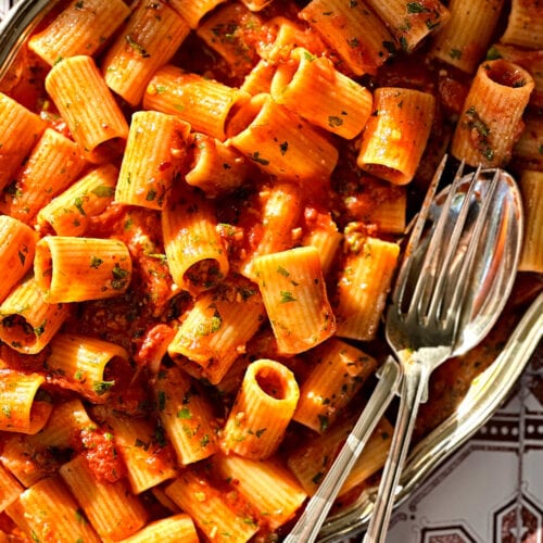 Rigatoni arrabbiata on a silver tray with a fork and spoon next to it.