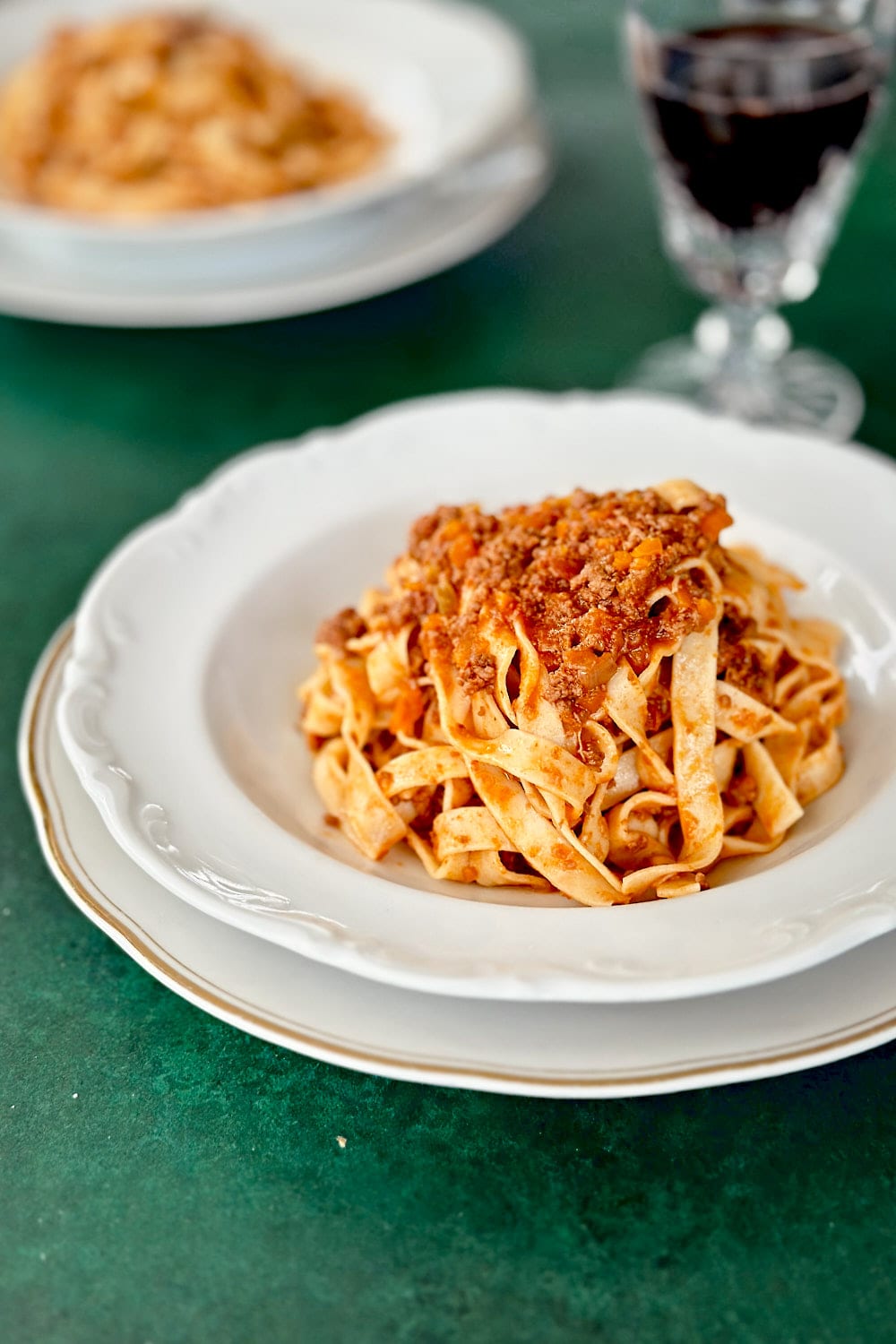 Two portions of homemade tagliatelle alla bolognese on a dark green table.