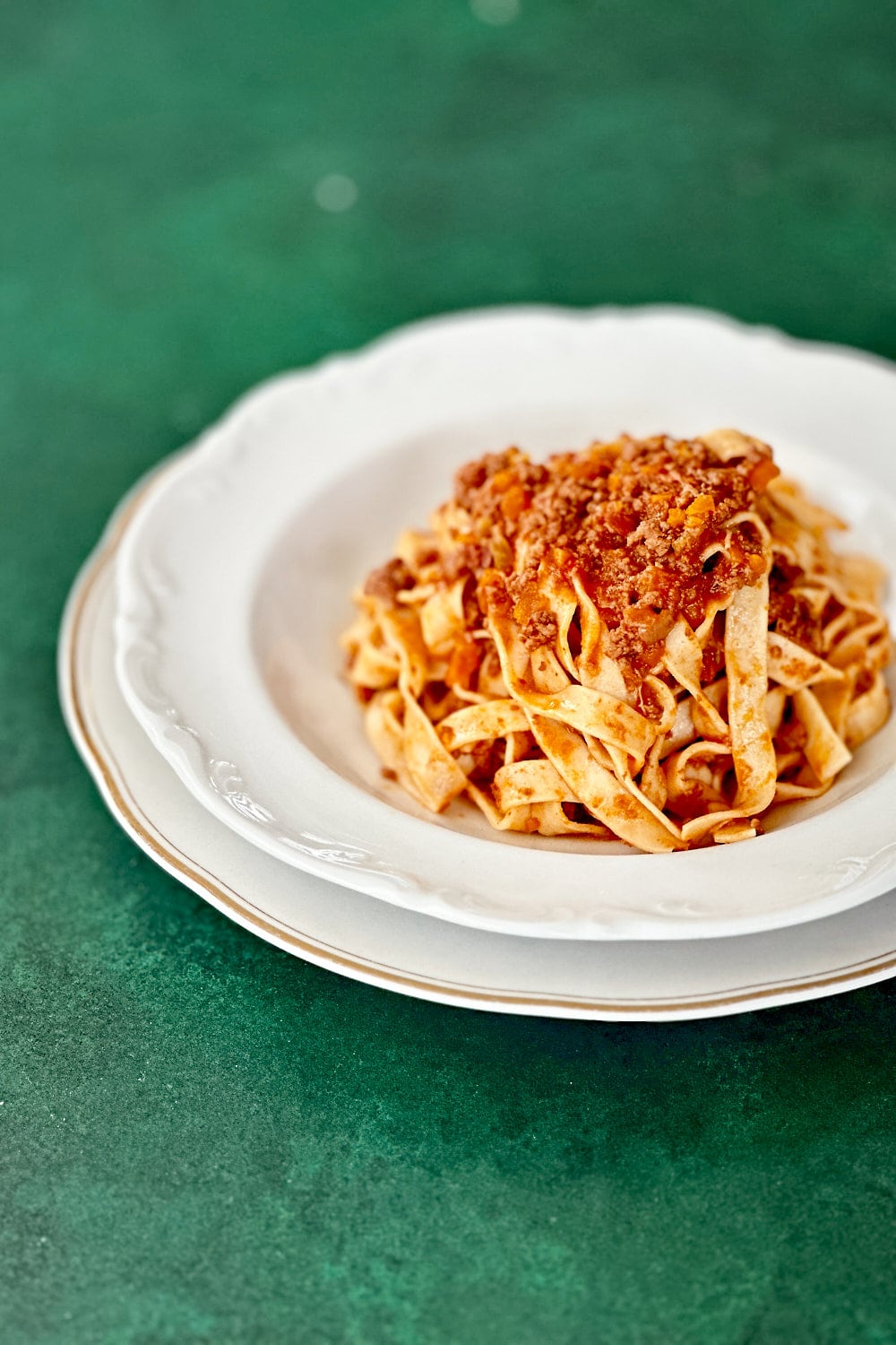 Homemade tagliatelle pasta with classic ragù alla bolognese on a white plate on a dark green backdrop.