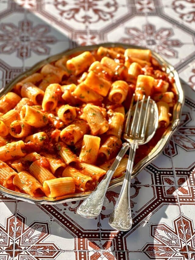 Rigatoni all'arrabbiata on a silver plate with a fork and spoon to serve it.