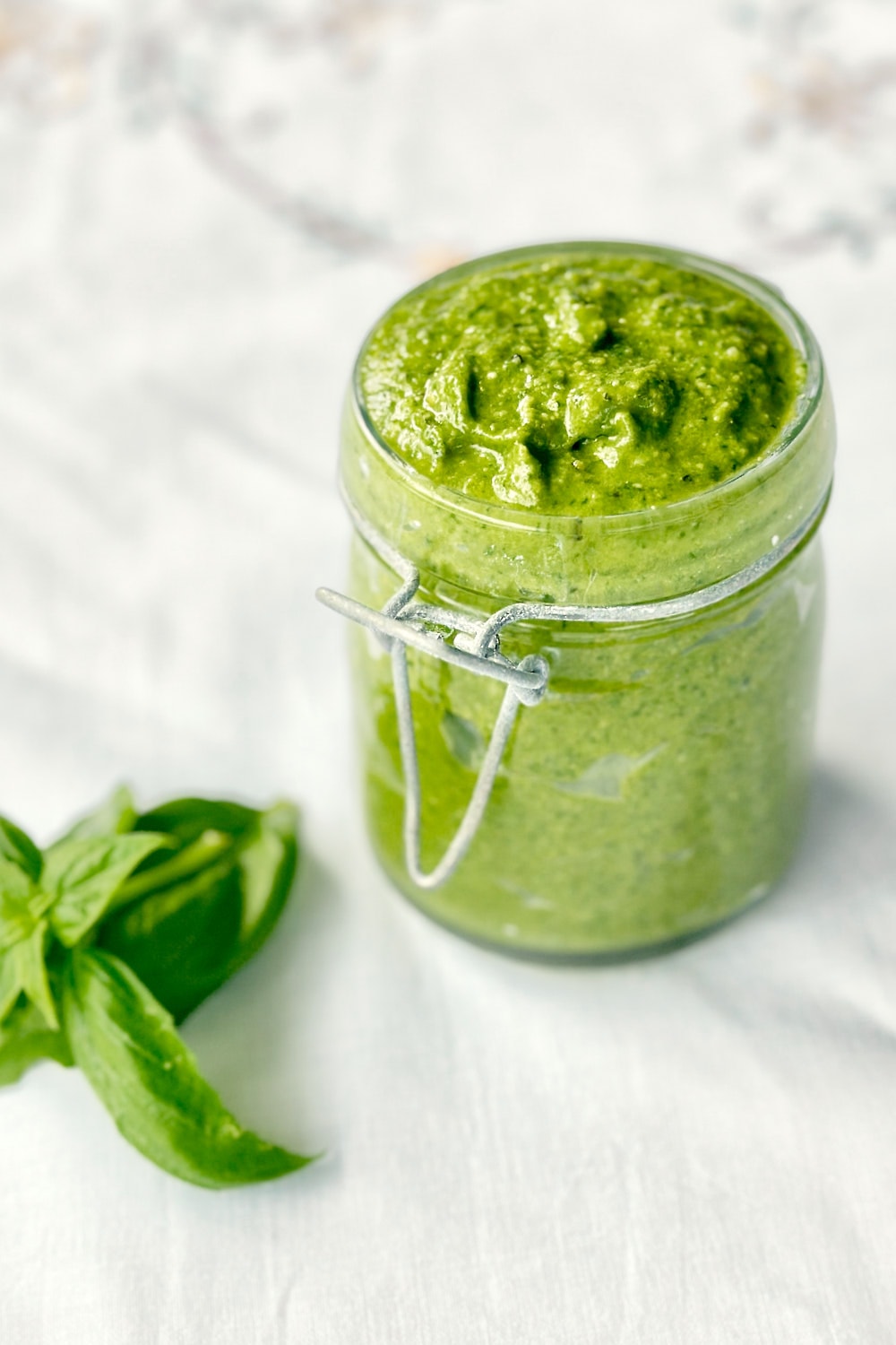 Homemade spinach and basil pesto with a vibrant green color in a small mason jar.