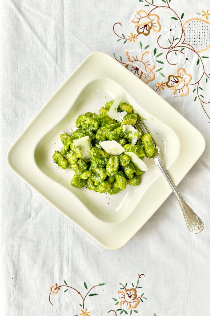 Creamy pesto gnocchi on a white plate placed on a white linen tablecloth.