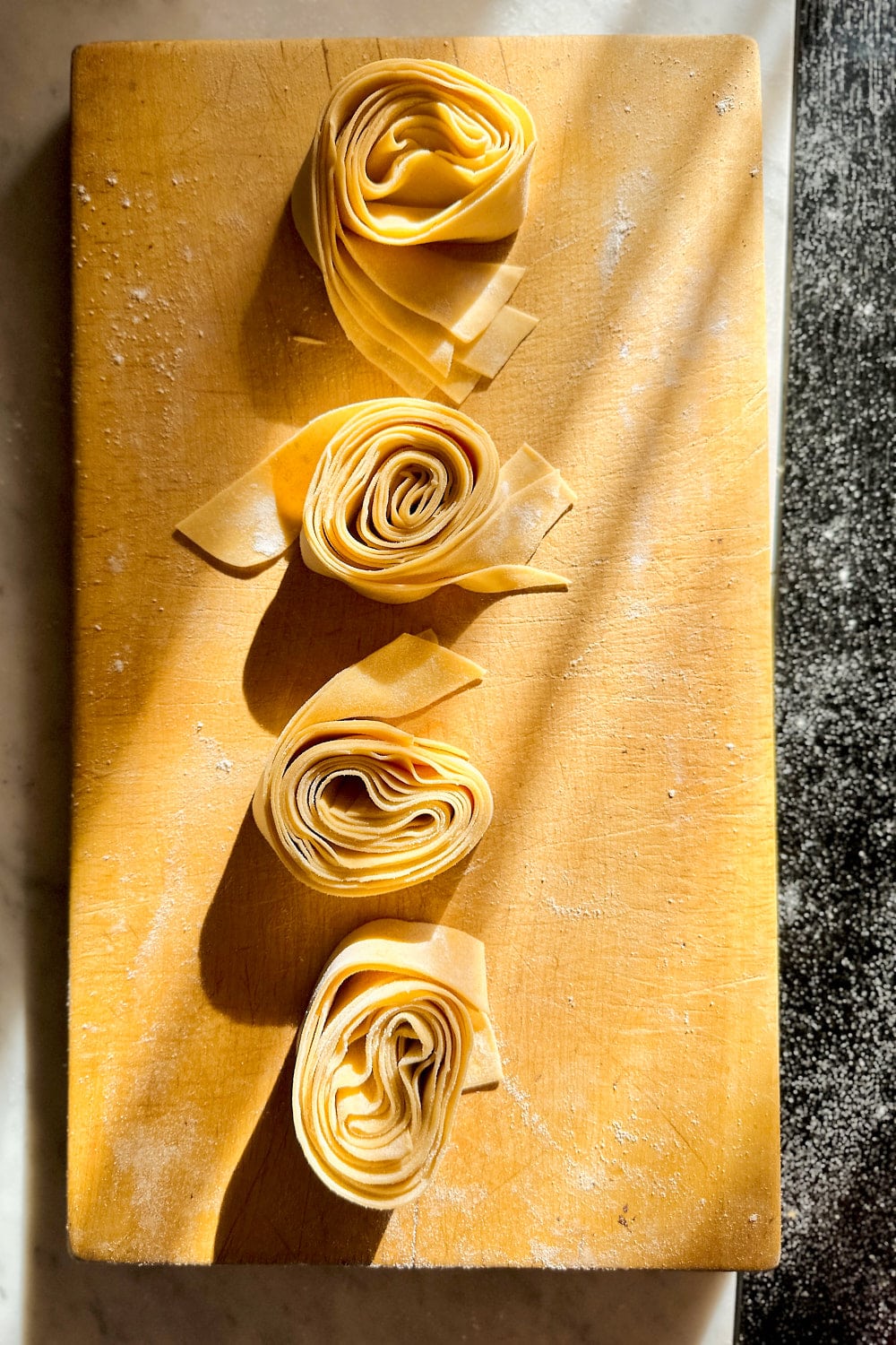 Four pasta nests of hand-cut pappardelle pasta on a wooden board.