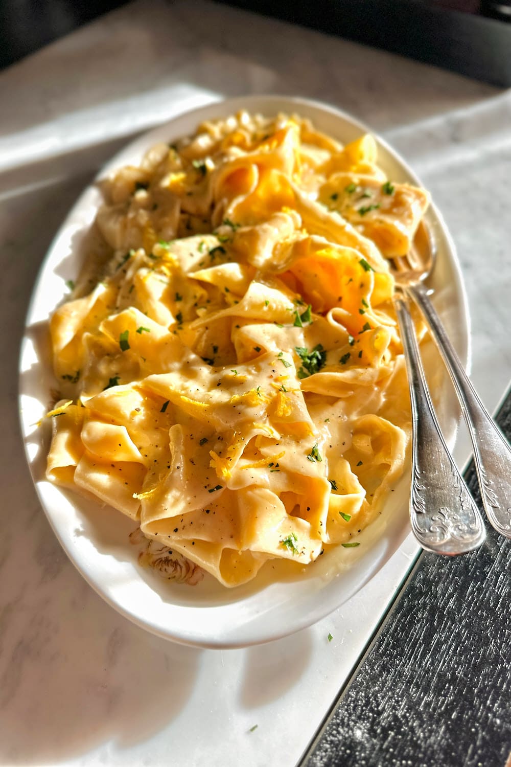 A white serving plate with homemade pappardelle al limone on a white marble table.